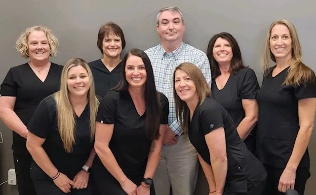 The dental team at Lonnie R. Harrison, DMD, eight staff members wearing black scrubs in the office
